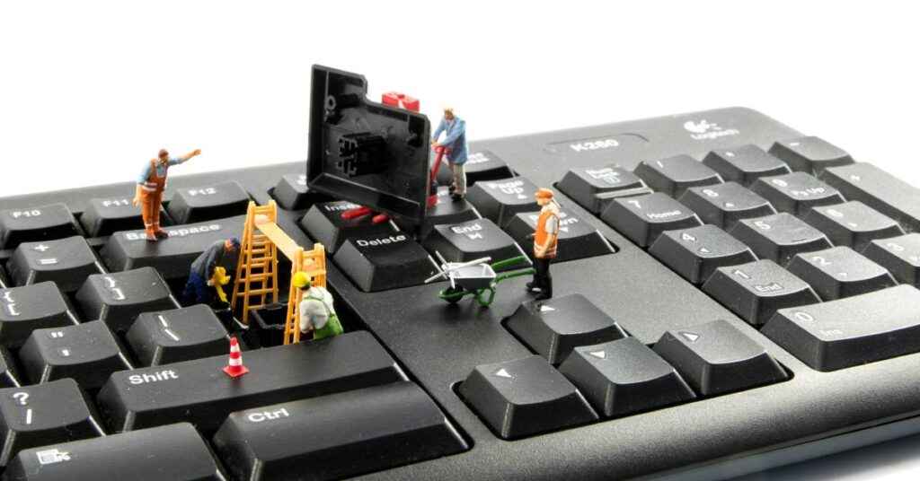 A close-up of little construction worker figurines on a block keyboard lifting up the enter key.