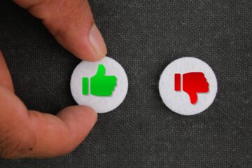 A close-up of a hand touching a thumbs-up button. There is a thumbs-down button next to it.