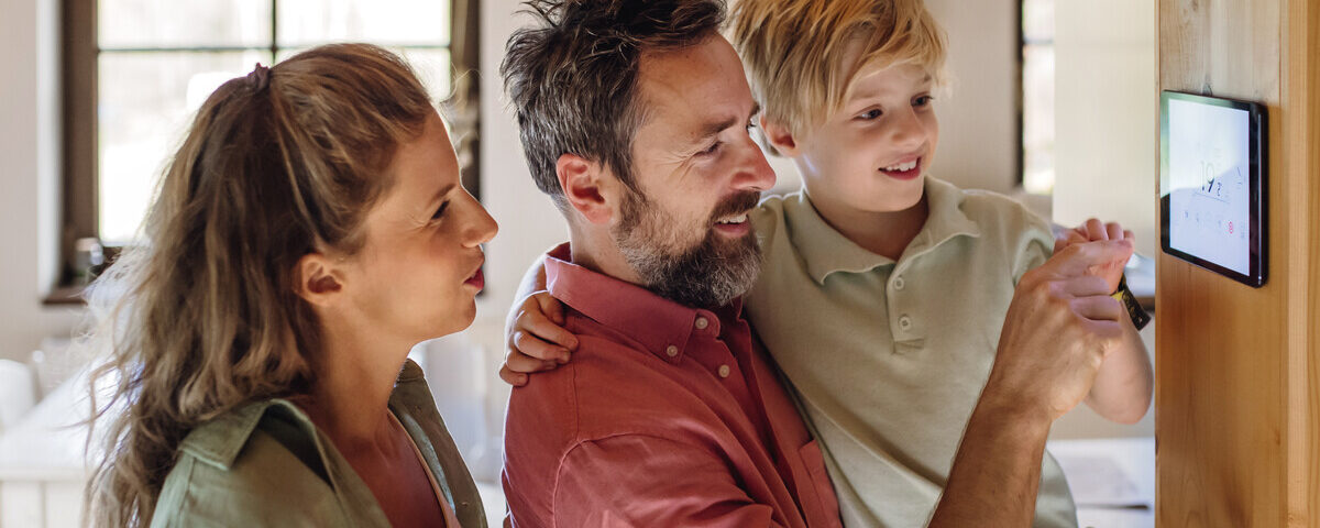 A man holding up a young boy and pointing to a touchscreen on the wall. A woman looks over the man's shoulder.